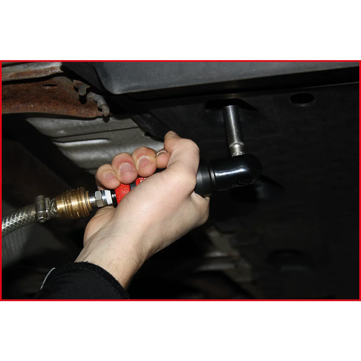 Eine Person hält einen schwarzen, rot umrandeten Druckluftschrauber. Ein Metallschlauch ist mit dem Werkzeug verbunden.